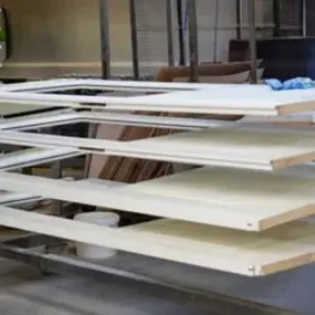 Mehrere lackierte Holzbretter trocknen auf einem Metallregal in einer Schreinerei.