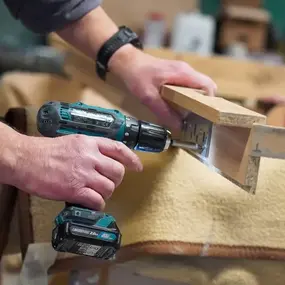 Ein Handwerker schraubt mit Akkuschrauber Holz auf Werkbank für Möbelbau zusammen.