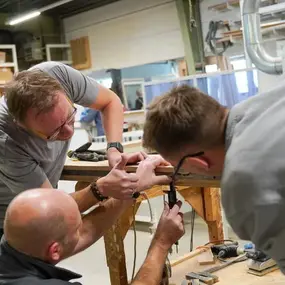 Drei Handwerker arbeiten gemeinsam an einem Holzprojekt in einer modernen Werkstatt.