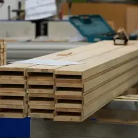 Gestapelte Holzbalken liegen in einer modernen Tischlerei auf einer Werkbank zur Verarbeitung.