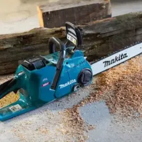 Makita Kettensäge liegt vor Holzscheit auf Boden, Holzspäne um die Motorsäge verteilt.