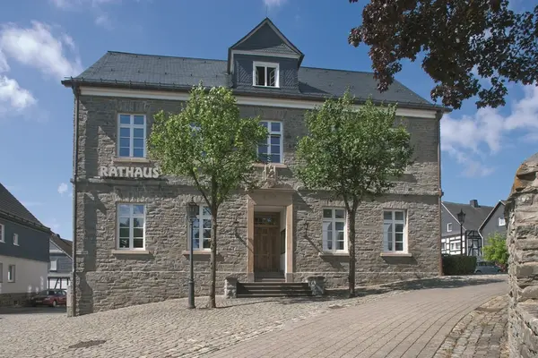Historisches Rathaus aus Stein mit Bäumen und Kopfsteinpflaster in einer Altstadt.