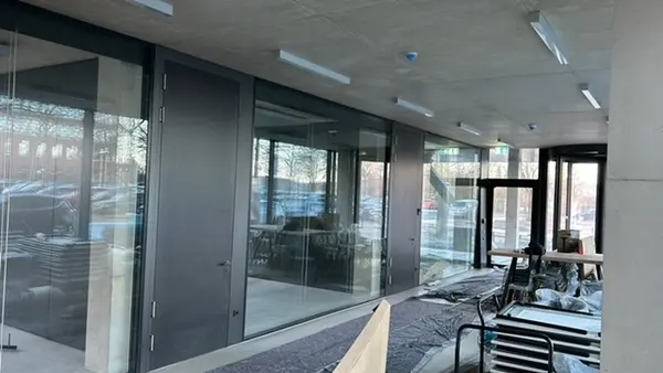 Moderner Bürogebäude-Eingang mit Glasfront, Baustellenmaterial und Tageslicht.