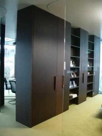 Modernes Büro mit großen, dunklen Holzregalen und Glastrennwand, Bücher und Ordner.