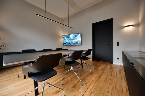 Moderner Konferenzraum mit Holzboden, großem Tisch, Designstühlen und Bildschirm.