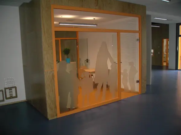 Besprechungsraum mit Glaswänden und Milchglasfolien mit Kinder- und Erwachsenenmotiven.