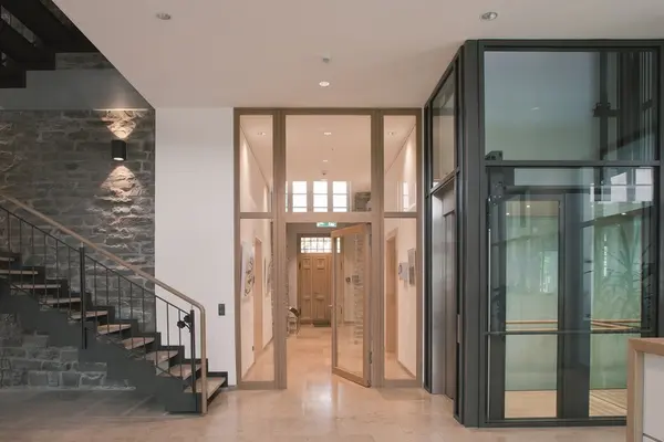 Moderner Eingangsbereich mit Aufzug, Natursteinwand und Treppenhaus in einem Bürogebäude.