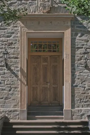 Historische Holztür in Sandsteinfassade mit Laternen, Eingang eines alten Gebäudes.