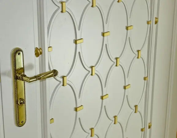 Weiße Zimmertür mit goldenen Verzierungen und elegantem Messing-Türgriff im Detail.